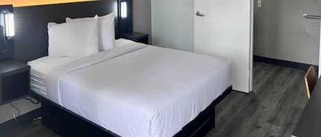 Una habitación de hotel con una cama grande, una mesita de noche, una lámpara de pared y una puerta.