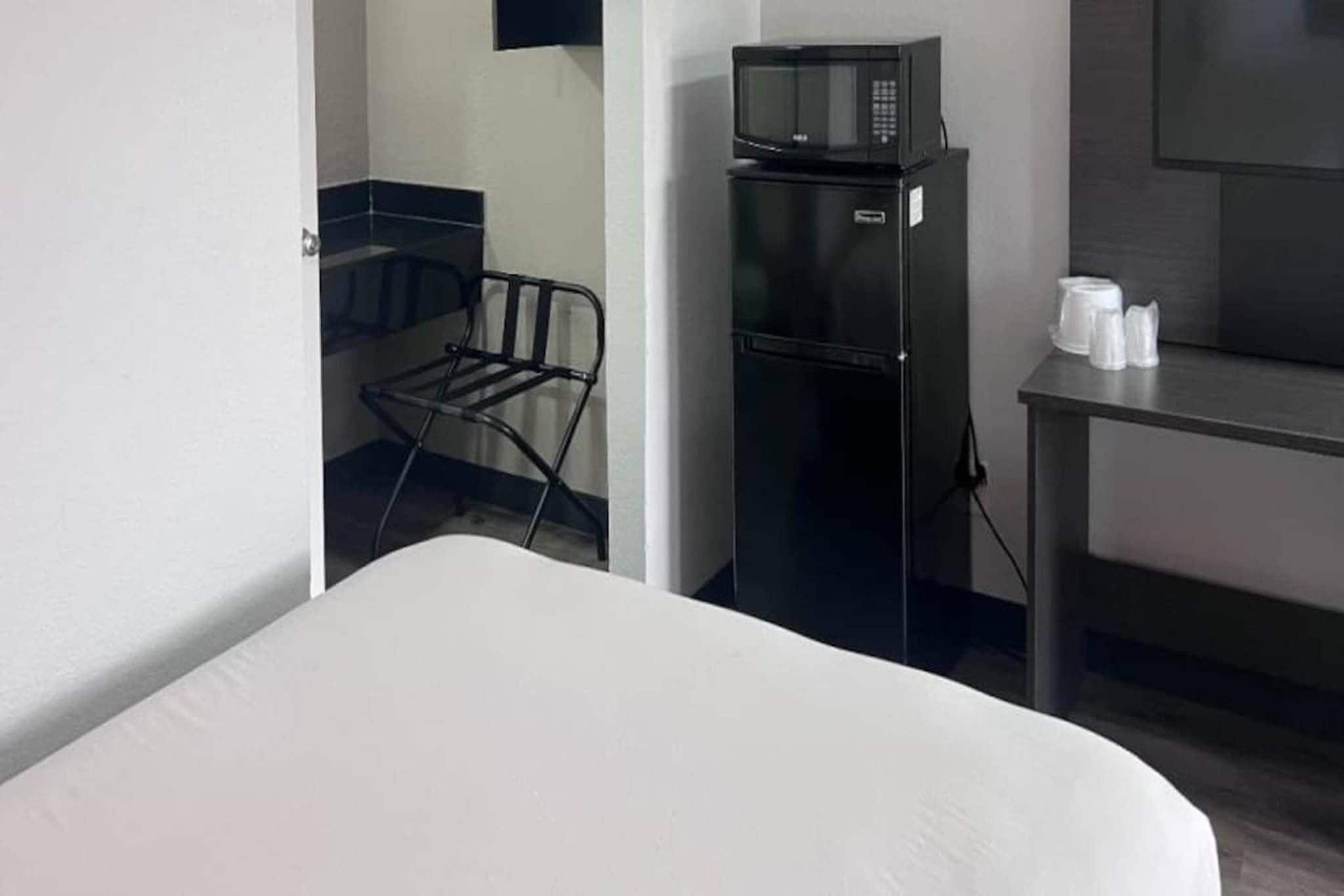 A hotel room with a bed, a microwave, a refrigerator, a chair, and a small table with cups.