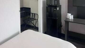 A hotel room with a bed, a microwave, a refrigerator, a chair, and a small table with cups.