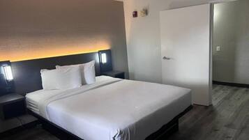 A hotel room with a bed, bedside tables, a nightstand, a wall-mounted lamp, and a wardrobe.