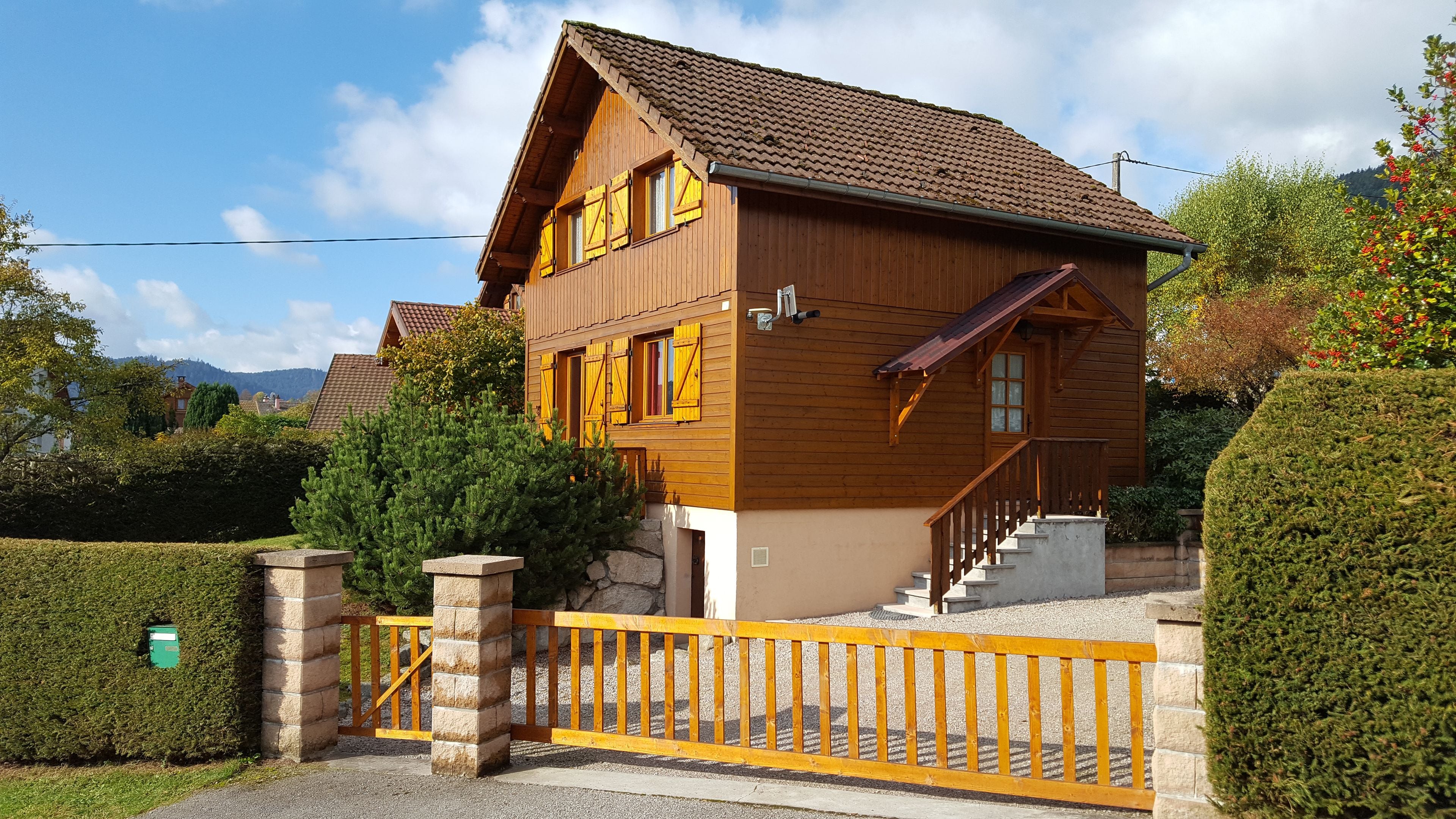 A two-story wooden house with a tiled roof, a gated entrance, and a stone staircase leading to the main door.