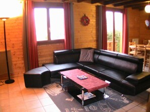 A living room with a black leather sofa, a red coffee table, and a patterned rug. - 3-Star Chalet in Gérardmer with 3 Bedrooms (Gérardmer)