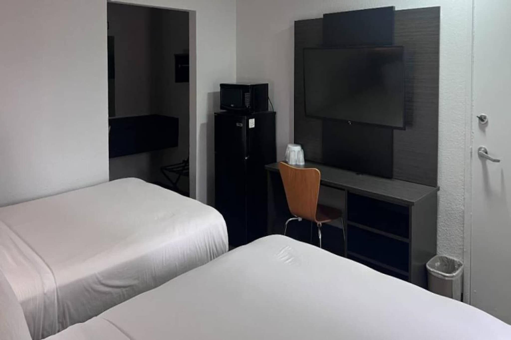 Ein Hotelzimmer mit zwei Betten, einem Schreibtisch mit Stuhl, einem Fernseher und einem Kühlschrank.