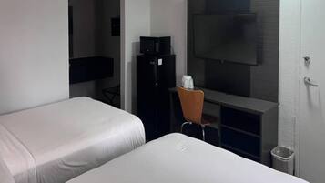 Ein Hotelzimmer mit zwei Betten, einem Schreibtisch mit Stuhl, einem Fernseher und einem Kühlschrank.