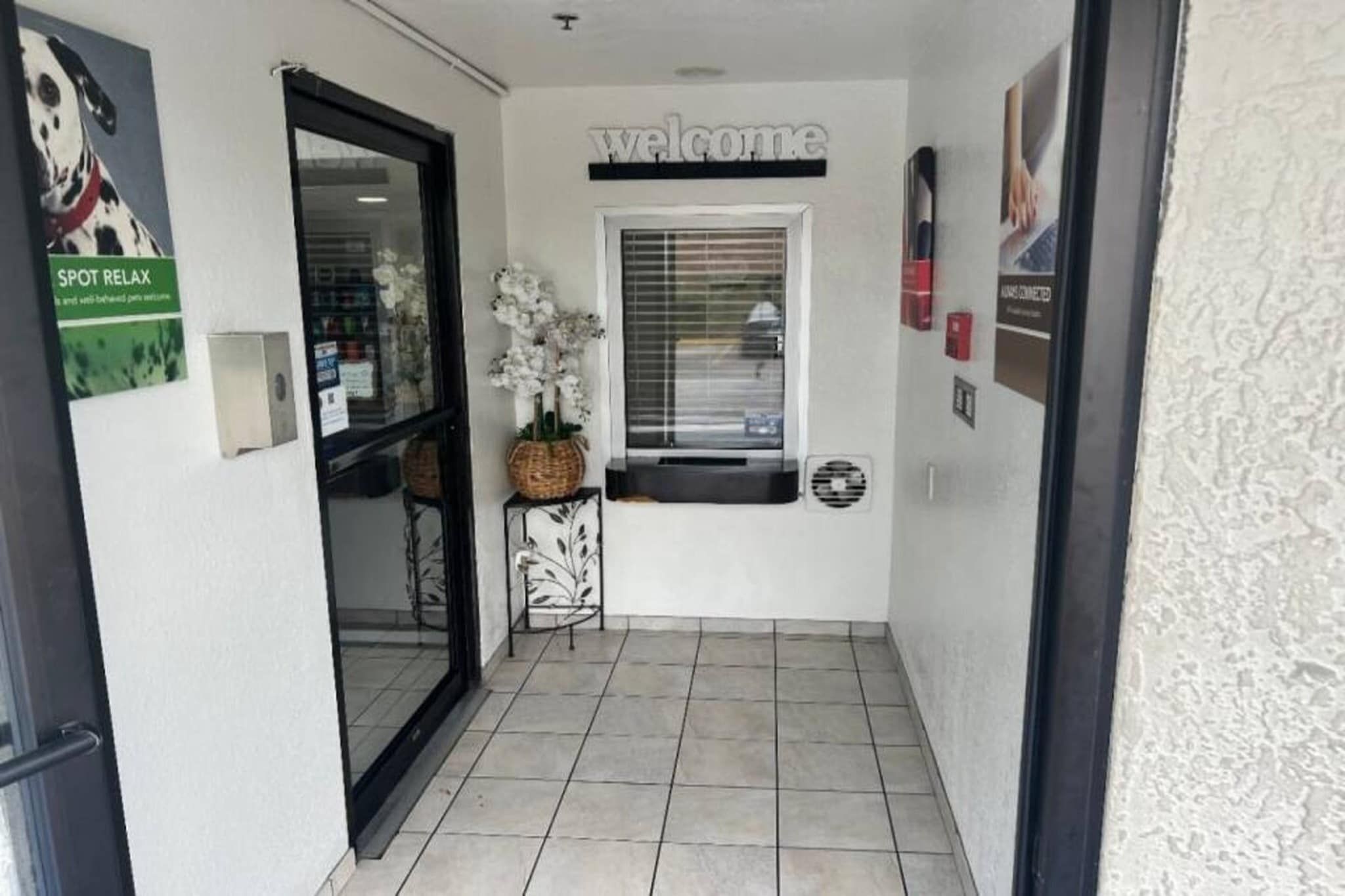 A hallway with a 'Welcome' sign, a window with blinds, a door, and a 'SPOT RELAX' sign.