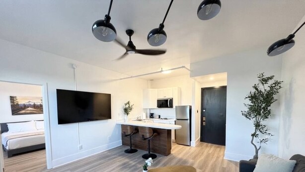 Een moderne woonkamer met een flatscreen televisie, een salontafel, een bank en een eethoek, met een keuken op de achtergrond.