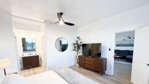 Een slaapkamer met een bed, een kaptafel, een spiegel, een televisie en een plafondventilator.