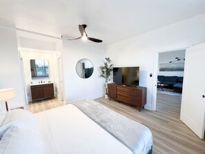 Un dormitorio con una cama, un aparador, un espejo, un televisor y un ventilador de techo.