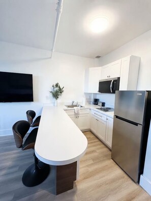 Una cocina moderna con una isla central, armarios blancos, electrodomésticos de acero inoxidable y un televisor de pantalla plana montado en la pared.