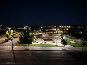 Una plaza urbana bien iluminada, con una fuente central, árboles y farolas.
