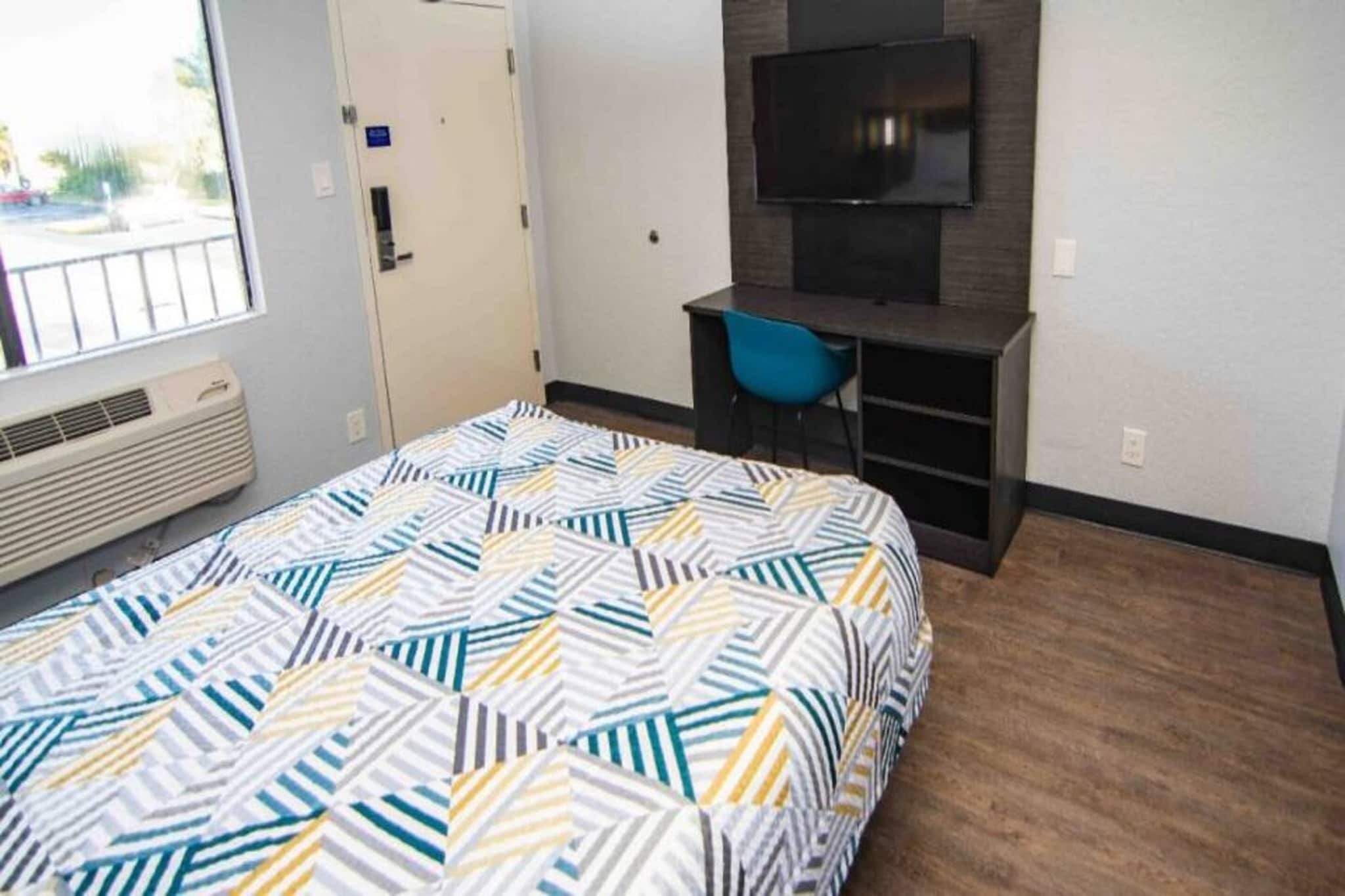 Een slaapkamer met een bed, een bureau, een stoel, een televisie en een raam.
