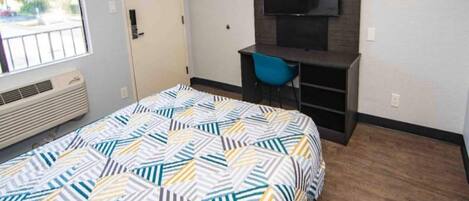A bedroom with a bed, a desk, a chair, a television, and a window.
