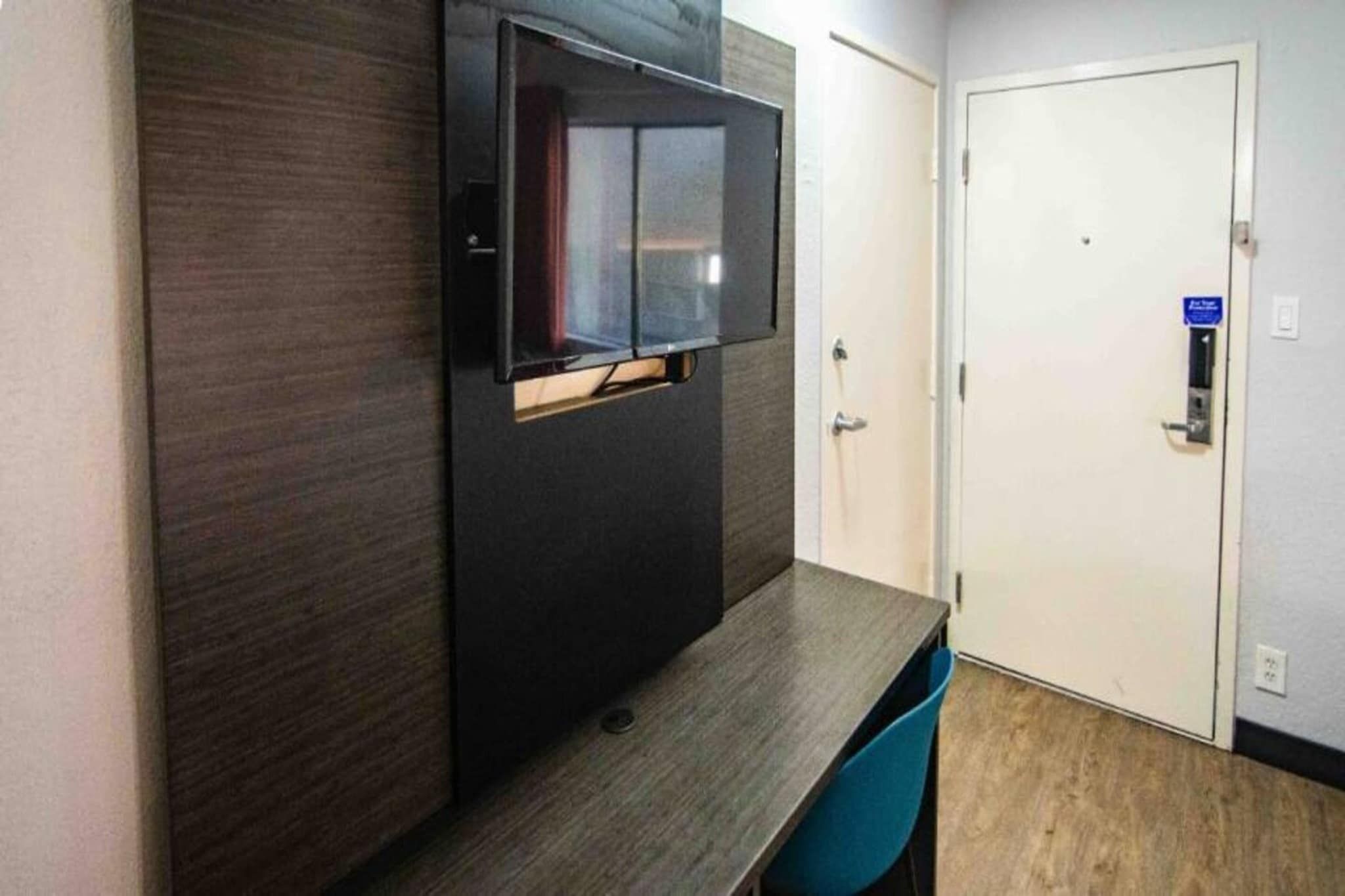 Een kamer met een wand bekleed met donker hout, een flatscreen televisie die aan de wand is bevestigd, een houten tafel en een blauwe stoel.