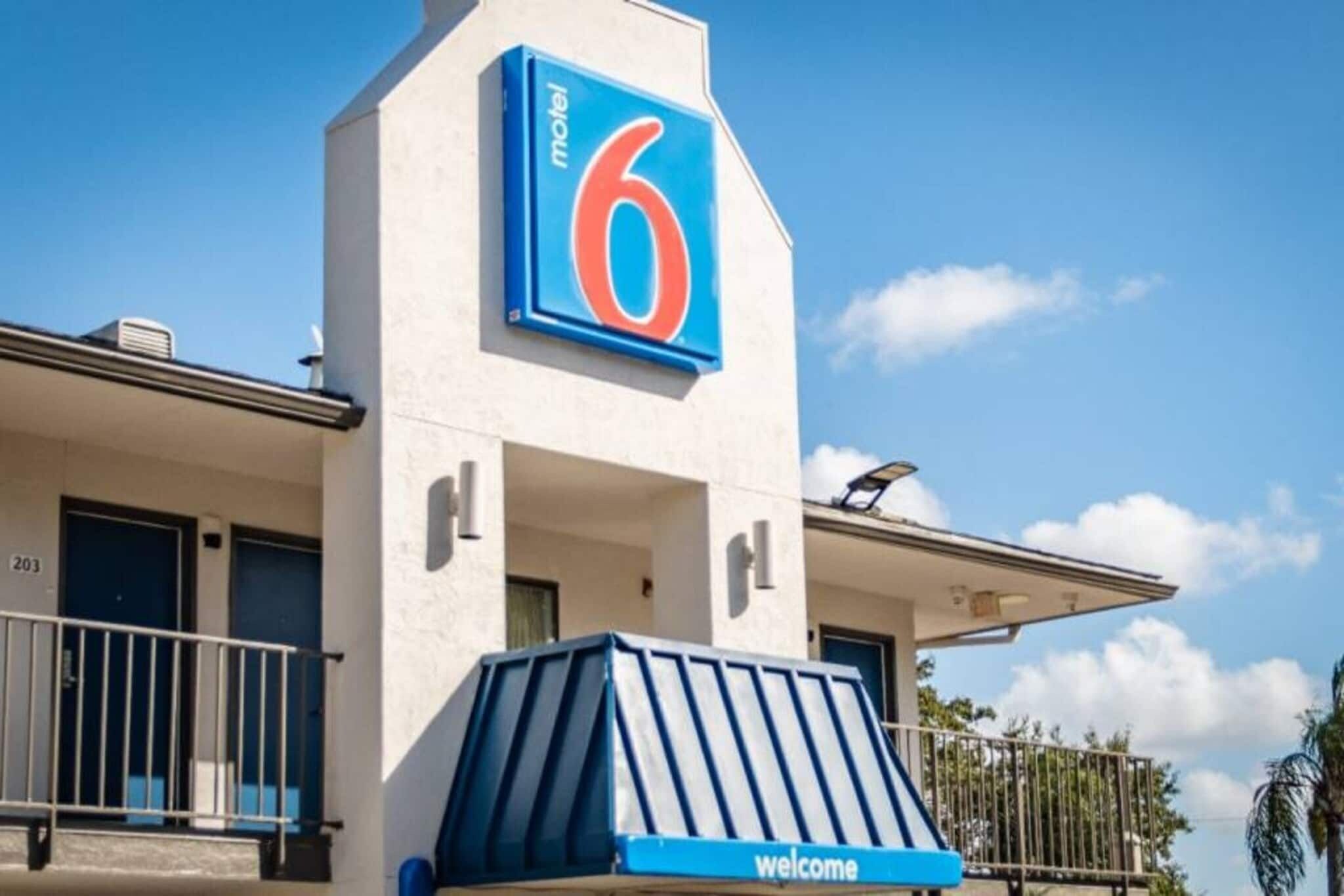 A motel with a prominent '6' sign, a 'welcome' sign, and a balcony with railings.