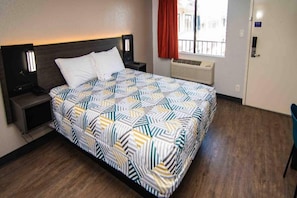 A hotel room with a bed, a nightstand, a bedside table, a window with a view, and a door. - Motel 6 Ft. Pierce, Fl_1 Queen Bed | Ada (Fort Pierce)