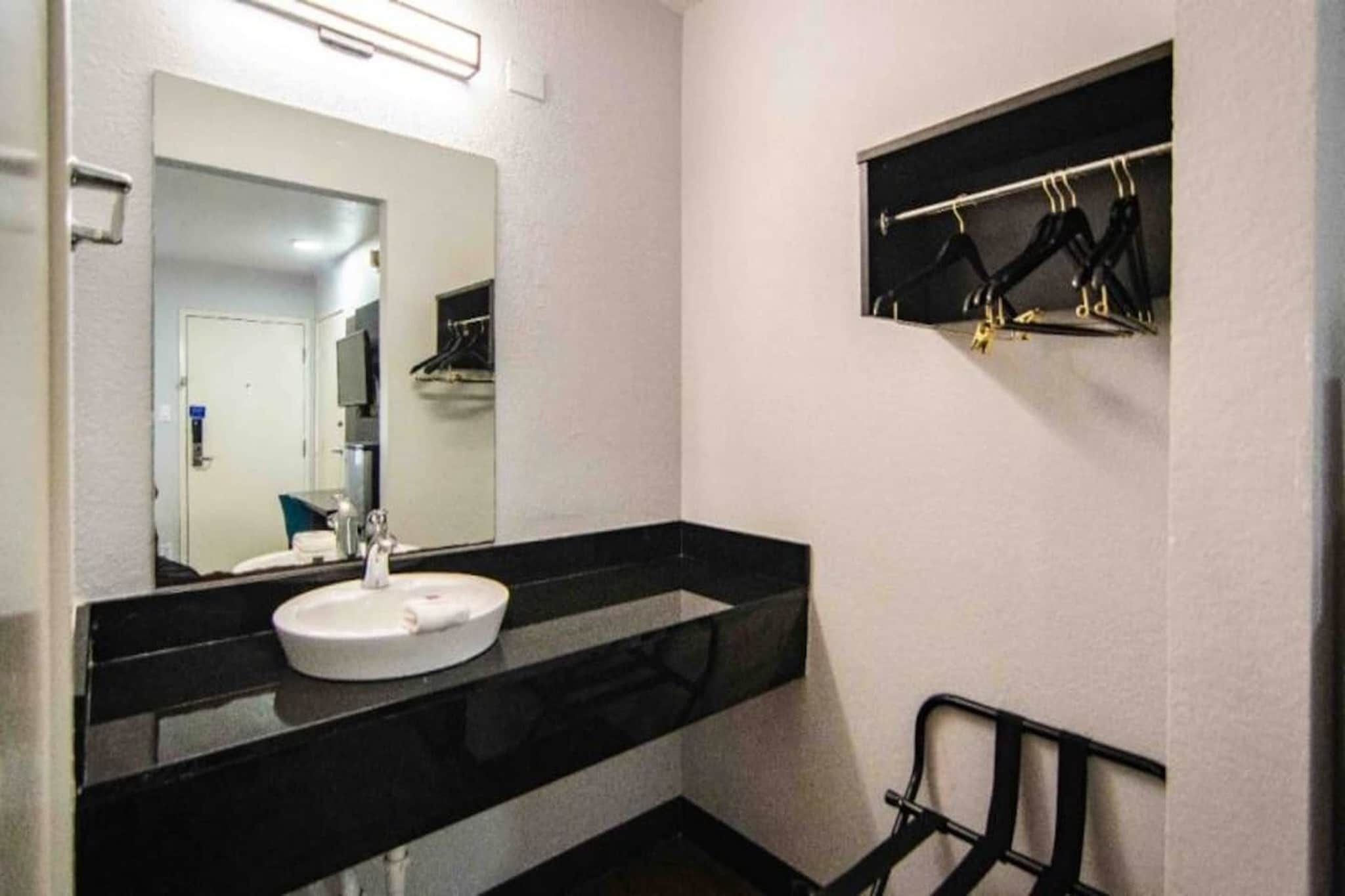 A bathroom with a white sink, a mirror, and a black towel rack.
