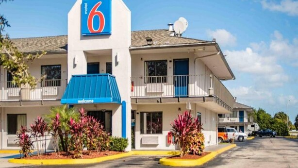 Um motel com um grande letreiro em formato de '6', toldo azul e estacionamento.