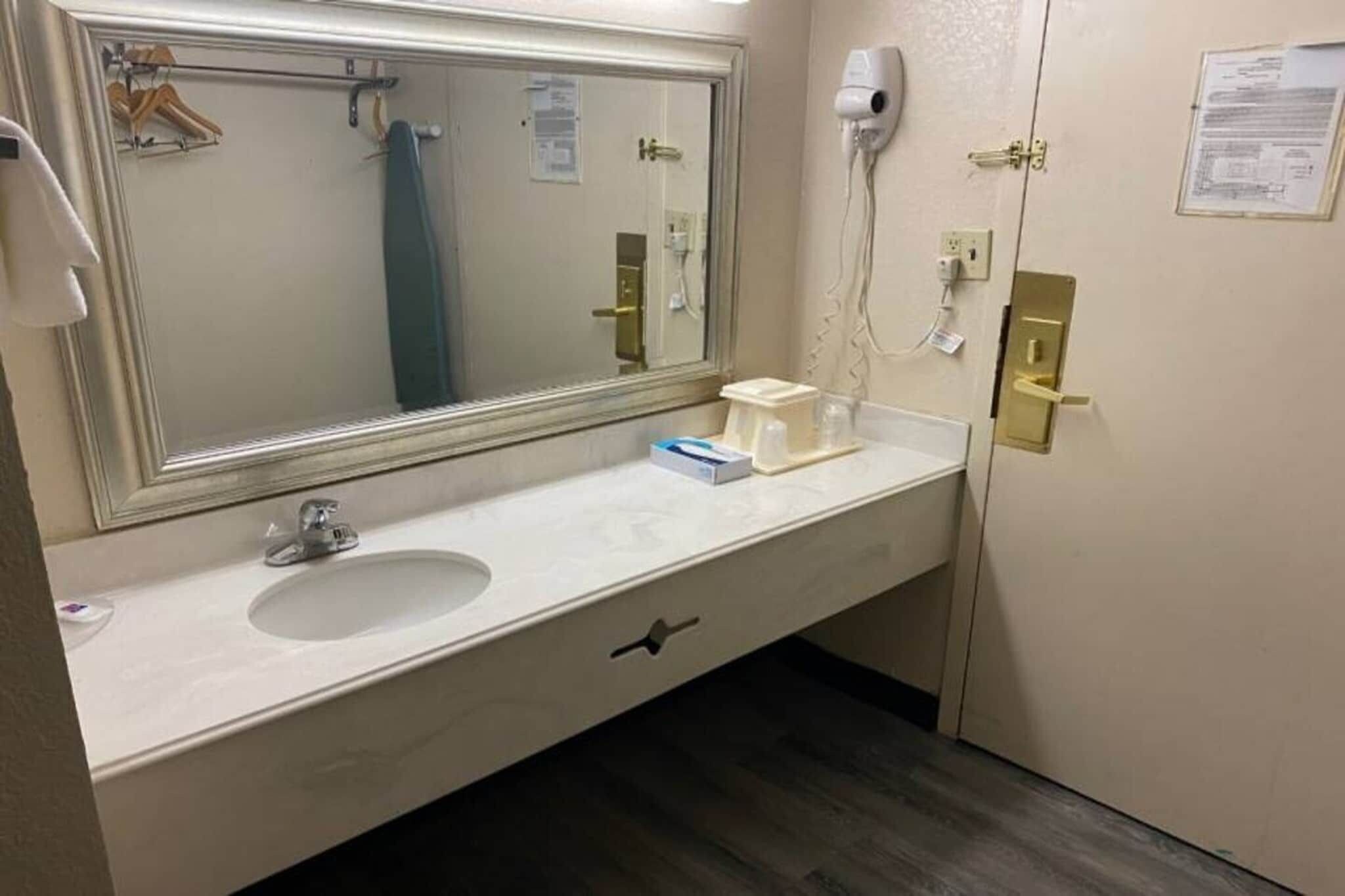 Een hotelbadkamer met een grote spiegel, een wastafel, een handdoekrek, een haardroger en een toilet.