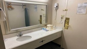 Casa de banho de hotel com um espelho grande, uma pia, um porta-toalhas, um secador de cabelo e uma sanita.