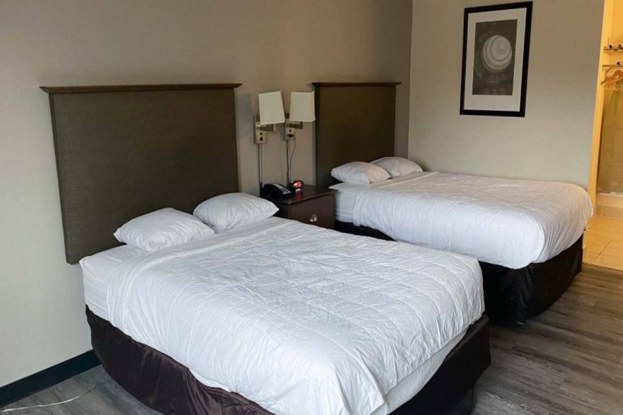 Ett hotellrum med två separata sängar, ett nattduksbord, en vägglampa och en inramad tavla.