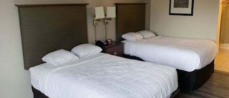Quarto de hotel com duas camas de solteiro, mesa de cabeceira, luminária na parede e um quadro emoldurado.