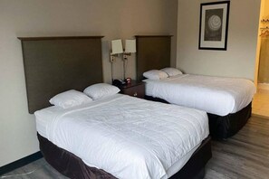 A hotel room with two single beds, a nightstand, a wall-mounted lamp, and a framed picture. - 2 Full Beds | Non-Smoking (Rochester NY)