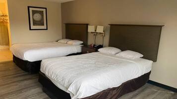 A hotel room with two beds, a nightstand, a lamp, and a framed picture on the wall.