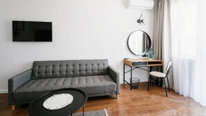 Una sala de estar moderna con un sofá gris, un espejo redondo, un televisor montado en la pared y un escritorio con una silla.