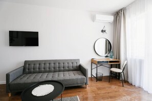 Una sala de estar moderna con un sofá gris, un espejo redondo, un televisor montado en la pared y un escritorio con una silla.