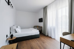 A hotel room with a bed, a desk, a chair, a TV, and a window with curtains. - Hotel Sozopol 99 (Sozopol)