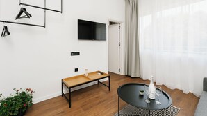 Una sala de estar moderna con un televisor de pantalla plana, un banco de madera, una mesita con copas de vino y una planta en maceta.