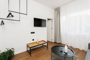 Una sala de estar moderna con un televisor de pantalla plana, un banco de madera, una mesita con copas de vino y una planta en maceta.