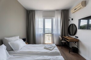 A hotel room with a bed, a desk, a chair, a TV, and a view of the sea. - Hotel Sozopol 99 (Sozopol)