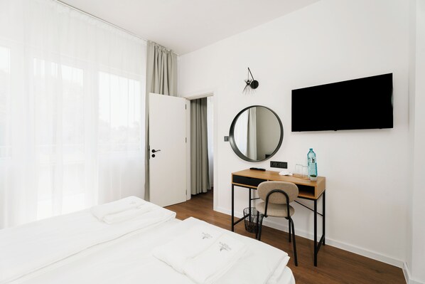 A hotel room with a bed, a desk, a chair, a mirror, a television, and a window with curtains.