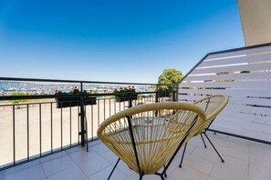 Un balcón con dos sillones de mimbre, barandilla y vistas al puerto deportivo.