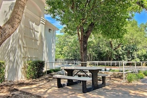 Une table de pique-nique dans un parc, avec un bâtiment blanc en arrière-plan.