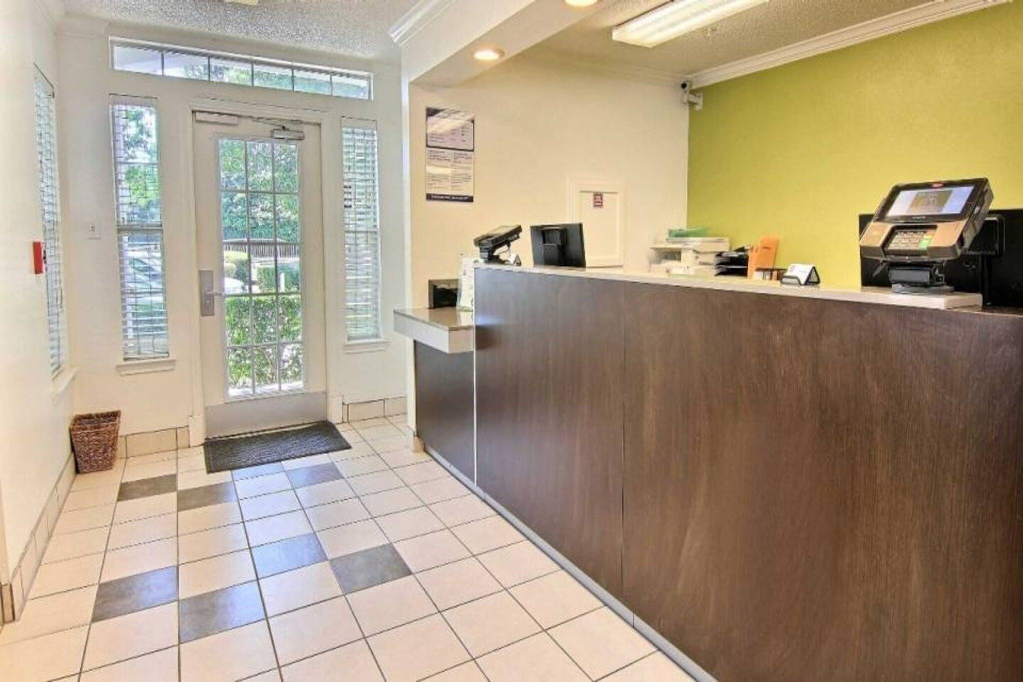 Un área de recepción con mostrador de entrada, una puerta que da al exterior y piso de baldosas.