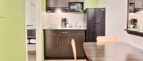 A compact kitchen with dark cabinets, a microwave, a refrigerator, and a coffee maker on the countertop.
