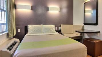 A hotel room with a bed, a chair, a small table, and a mirror.