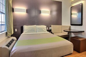 Een hotelkamer met een bed, een stoel, een klein tafeltje en een spiegel.