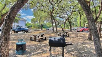 Un parque con mesas de picnic, una parrilla y árboles.