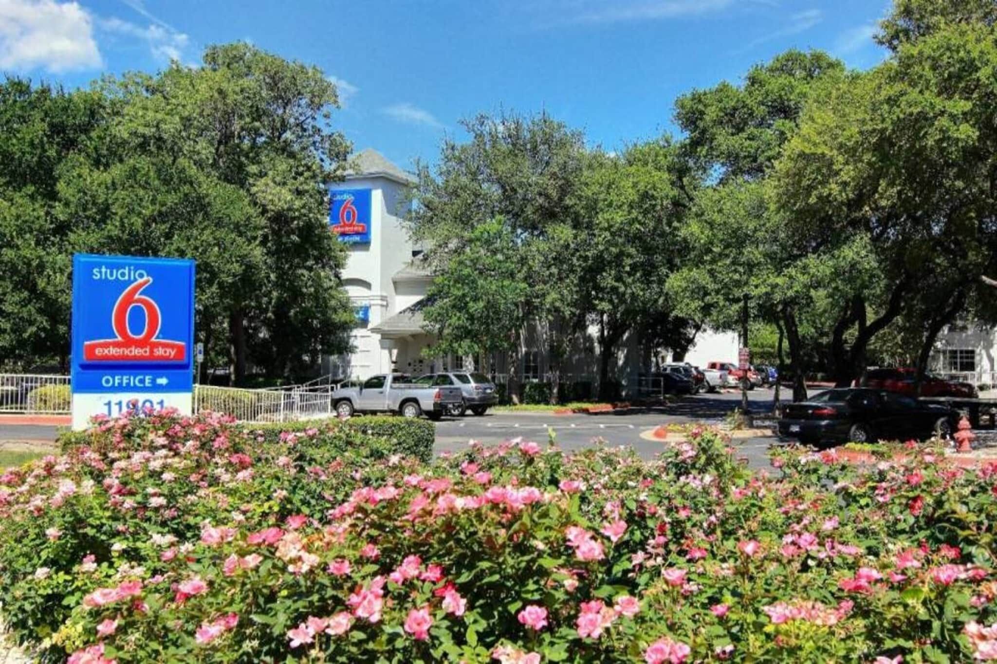 Skilt for et kontor til et udvidet opholds hotel, omgivet af frodig vegetation og parkerede biler.