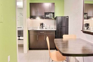 Una cucina compatta con mobili scuri, un forno a microonde, un frigorifero e una macchina da caffè sul piano di lavoro.