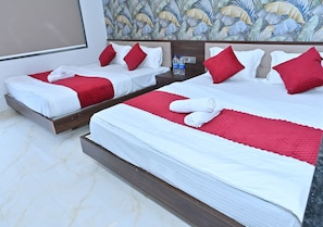 A hotel room with two beds, each with white linens and red pillows, a wooden headboard, and a floral wallpaper design.