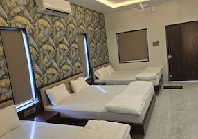 Quarto de hotel com quatro camas dispostas em linha, um espelho grande, um aparelho de ar condicionado e uma porta.