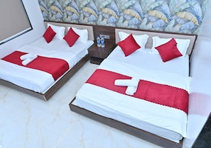 A hotel room with two beds, each with white bedding and red accents, a nightstand with water bottles, and a floral wallpaper design.
