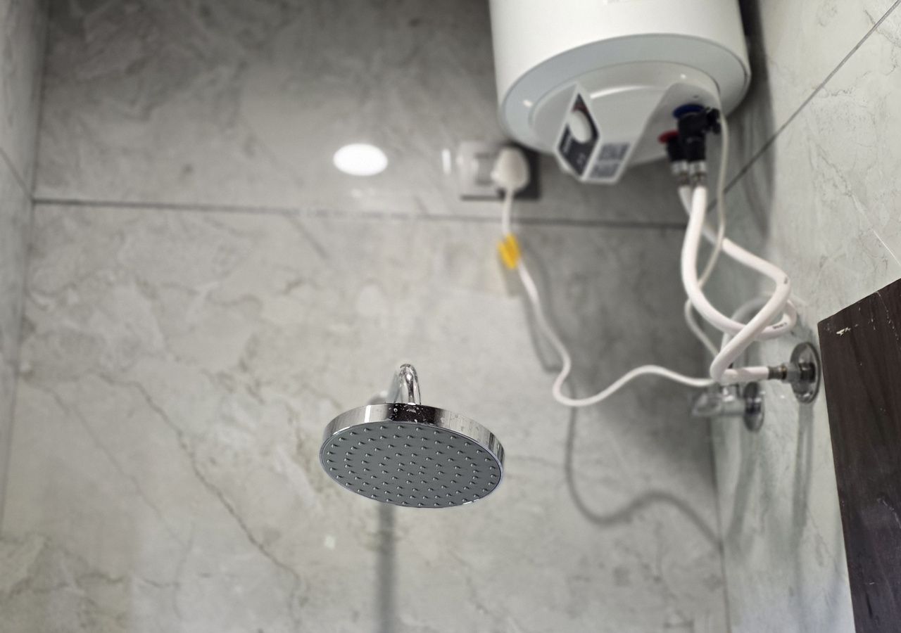 Un cabezal de ducha y un calentador de agua en un baño con piso de baldosas.