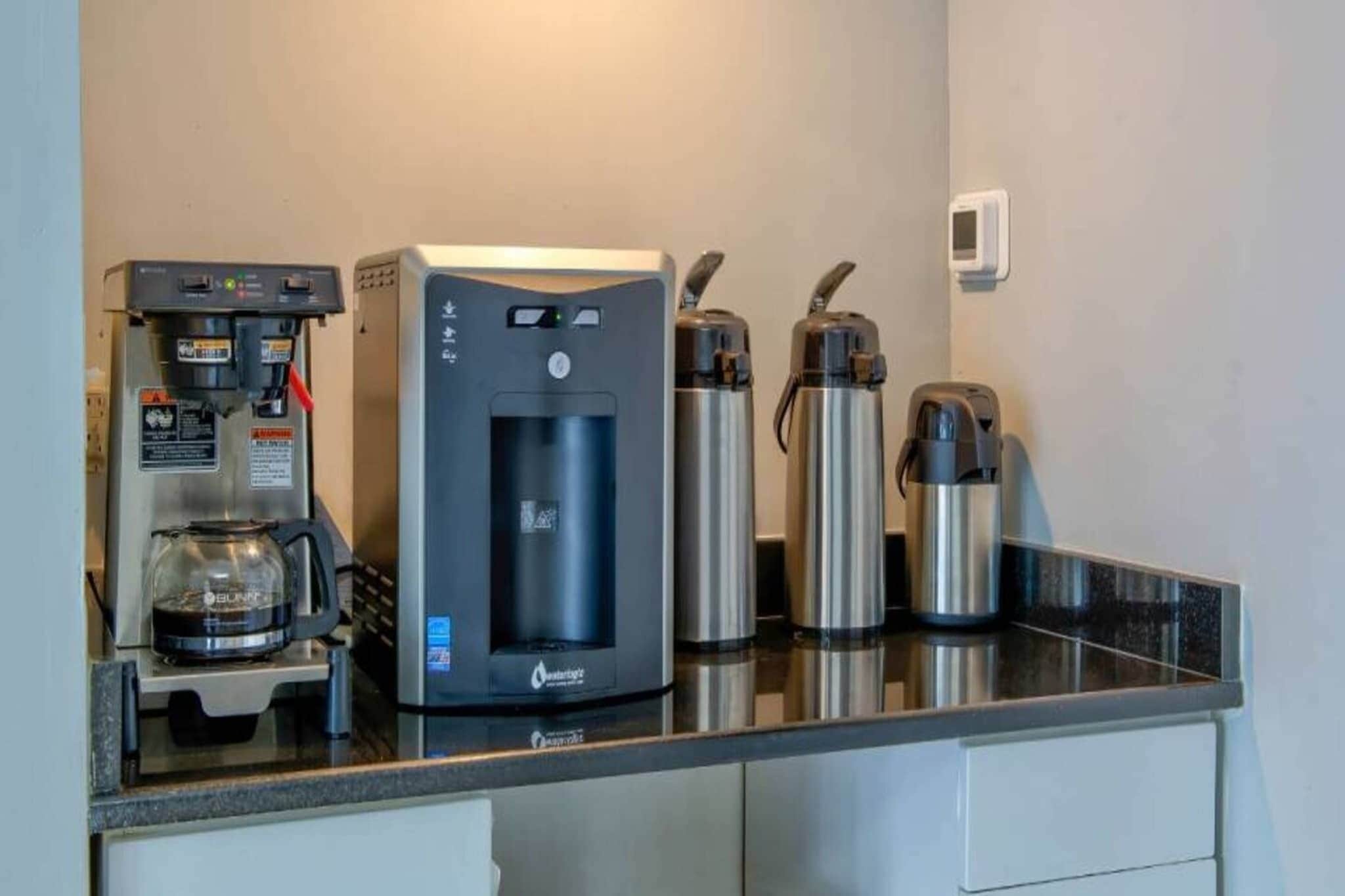 A kitchenette with a water dispenser, a coffee machine, and two stainless steel thermos cups.