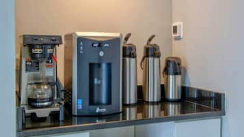 A kitchenette with a water dispenser, a coffee machine, and two stainless steel thermos cups.