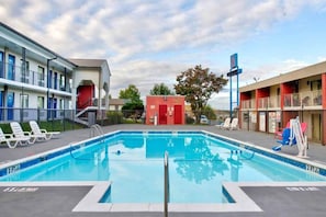 Une piscine dont la profondeur est indiquée à 3 pieds, entourée de chaises longues, d’un bâtiment rouge et d’un panneau bleu.